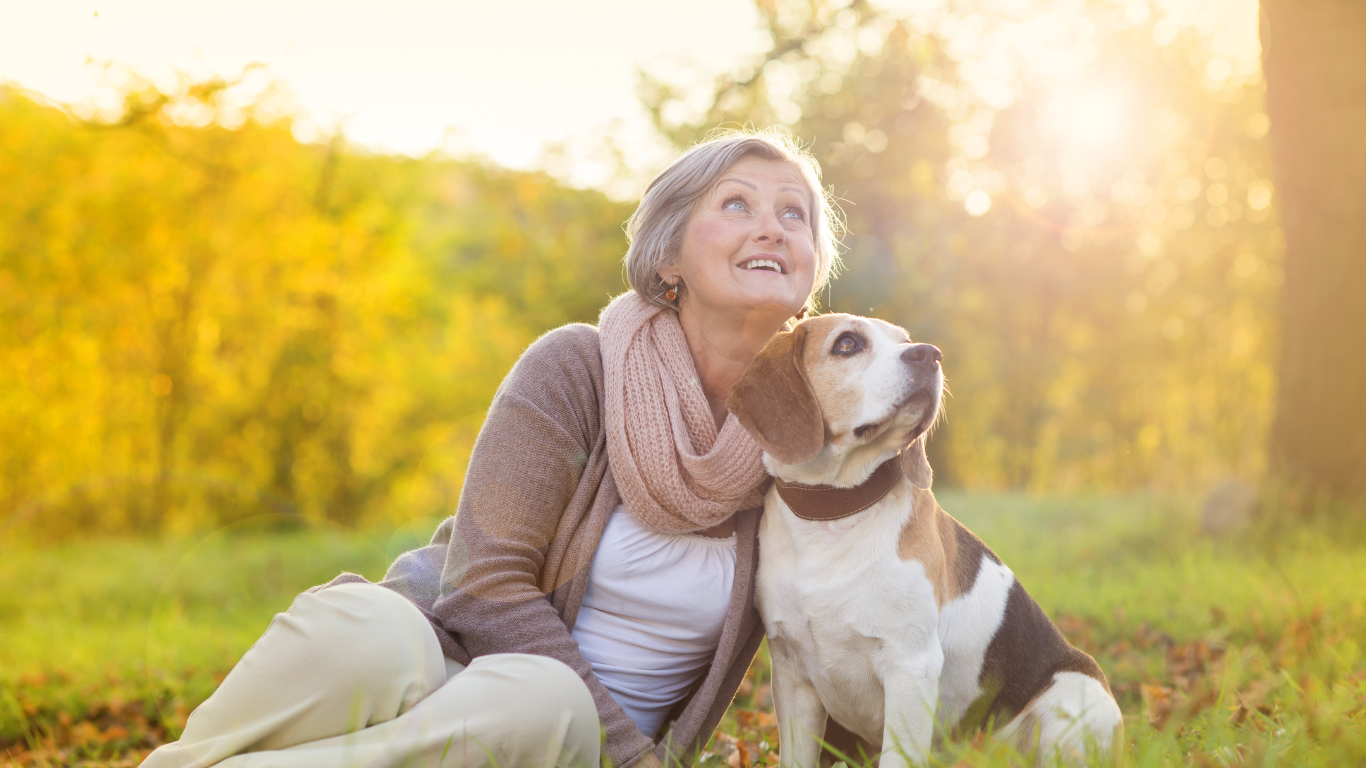 A senior woman poses for a photo with her mid-sized dog in a park