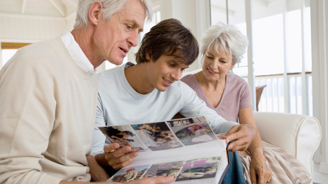 Two seniors sit down with their adult son and look at photo albums